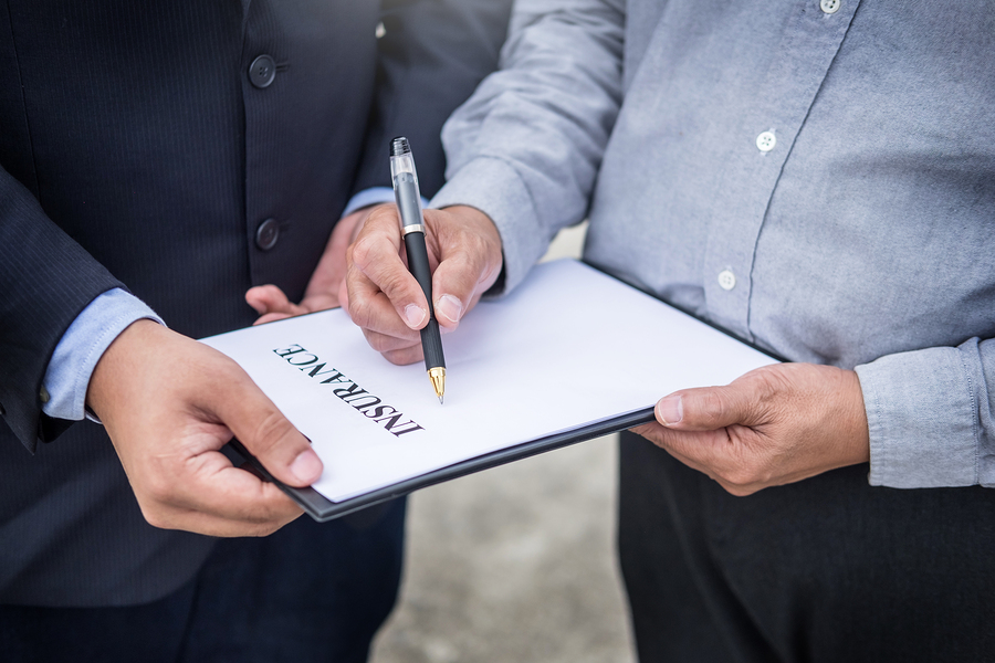 Car insurance agent send a pen to his customers sign the insurance form on clipboard while examining car after accident claim.